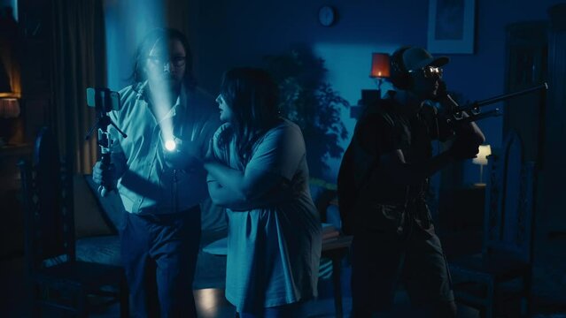 Zoom in video capturing two ghost hunters and a victim going around the room in search for the cause of a paranormal activity, using EMF detector and filming it.