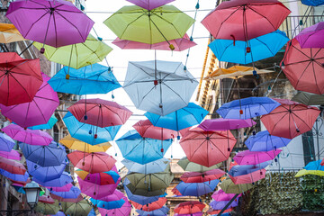 Fototapeta na wymiar Colorful Umbrellas of Catania's Streets - A shot of the bustling streets adorned with a cascade of suspended colorful umbrellas.