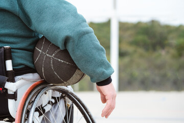 athlete in wheelchair holding ball under arm in basketball court