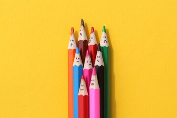 Multi-colored pencils with painted faces lie on a yellow background.	 - obrazy, fototapety, plakaty