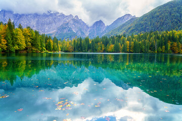 Laghi di Fusine inferior lake, Tarvisio, Italy. Amazing autumn landscape, crystal clear water with reflection and colored forest surrounded by Mangart mountain range, outdoor travel background - obrazy, fototapety, plakaty