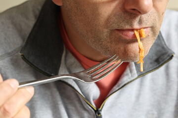 Close-up of the lower part of a man's face, sucking on a single cooked spaghetti strand while...