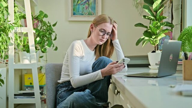 Serious teenage female sitting at home reading texting on smartphone