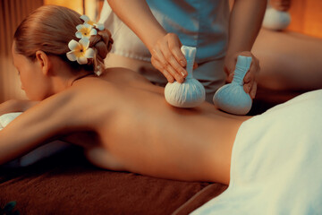 Hot herbal ball spa massage body treatment, masseur gently compresses herb bag on couple customer...