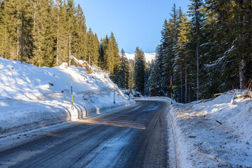 Icy mountain pass road though a snowy pine forest on a clear winter day