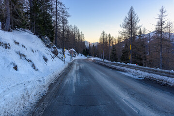 Icy winding alpine road through a snowy forest at dusk in winter