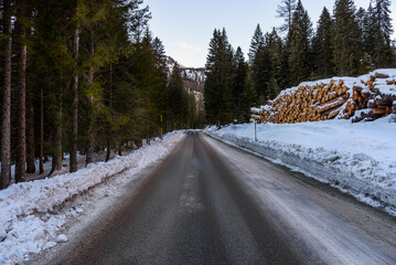 Deserted straight stretch of an icy mountain road running through a snowy forest at dusk in winter