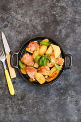 Fried chicken and potatoes on black plate on black background.