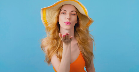 Flirt and woman in swimsuit sending air kiss, fashionable hat, smiling enjoys summertime for skincare, spa. Glamor flirty sexy slim lady for rest, tan, pool party concept on vivid blue background - obrazy, fototapety, plakaty