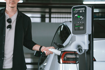 Young man travel with EV electric car to shopping center parking lot charging in downtown city...