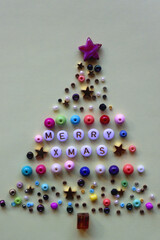 Various colorful beads with Merry Xmas caption on pastel yellow background. Beads arranged like Christmas tree. Top view.