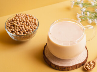 Organic soy milk in glass on wooden coasters and soybean in bowl on beige background. vegan product, Minimalist concept and Healthy drinks