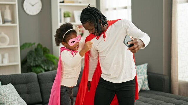African american father and daughter smiling confident wearing superhero costume make selfie by smartphone at home
