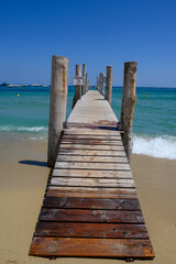 Fototapeta premium Wooden pier and crystal clear blue water of legendary Pampelonne beach near Saint-Tropez, summer vacation on French Riviera, France, text translation: it's dangerous not to dive from pier.
