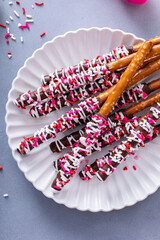 Chocolate dipped pretzel rods with pink heart sprinkles on a plate