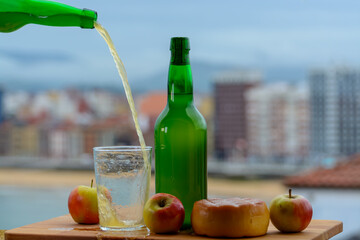 Traditional natural Asturian cider made from fermented apples in wooden barrels should be poured from great height for air bubbles into the drink and view on San Lorenzo beach of Gijon