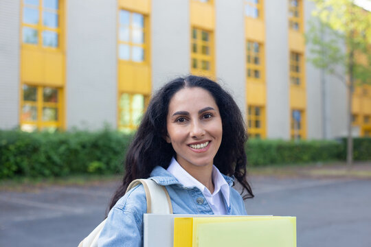 Shoulder length portrait of a high school girl walking to class with folders in her hands and backpack, turned and smiling, looking at camera, happy to be back at school. Educational institution.