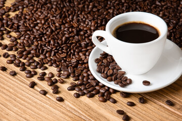 Scattered coffee beans and cup with coffee on wooden background