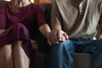 couple sitting on sofa holding hands  - obrazy, fototapety, plakaty