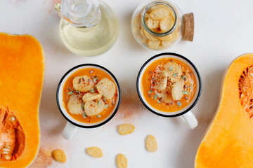 Roasted butternut squash soup with cream and pumpkin seeds on two white mugs.