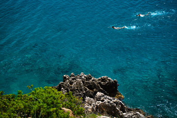 Steep rocky coast with swimmers in the sea © Zsuzsanna