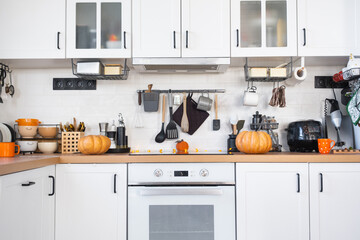 Decor of the white classic kitchen with pumpkins for Halloween and harvest. Autumn mood in the home interior, modern loft style.
