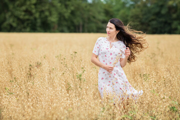 Fototapeta na wymiar Young woman in white midi dress walking across the field with ripe golden ears of chickpeas. Beauty Romantic woman Outdoors