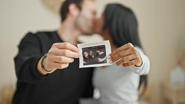 Beautiful couple sitting on bed holding baby ultrasound kissing at bedroom
