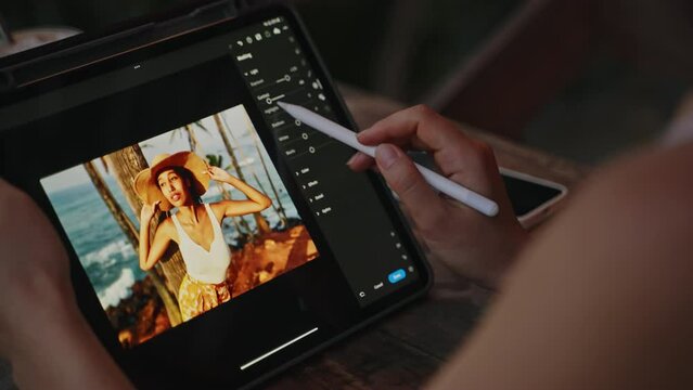 Female retoucher hands editing photo of girl on tablet. Freelancer working with stylus on gadget at the tropical cafe. SMM manager creates content. Business person on remote work day. Close-up.