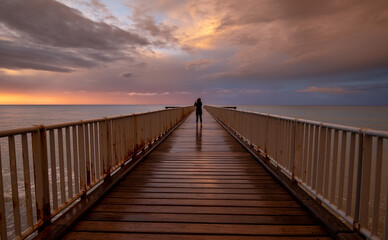 Fototapeta na wymiar Person standing alone on a pier enjoying dramatic sunset at the sea. Exploring nature. Dramatic light