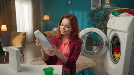 Redhead woman sitting next to a washing machine that just finished running, reading the instruction...