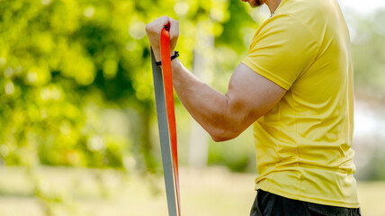 Man excercising with elastic rubber band outdoors making arm workout. Guy making fitness with sport equipment