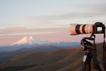 Evening photography. Camera with a long lens on a tripod. Snow-covered volcano peak in the...