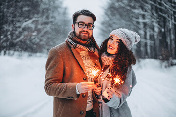 Happy young romantic couple have fun outdoors in winter with Bengal lights. Two lovers are hugging...