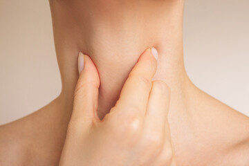 close-up of a young Caucasian woman experiencing sore throat when swallowing, suffering from thyroid diseases, pain in the trachea. Isolated on a beige background