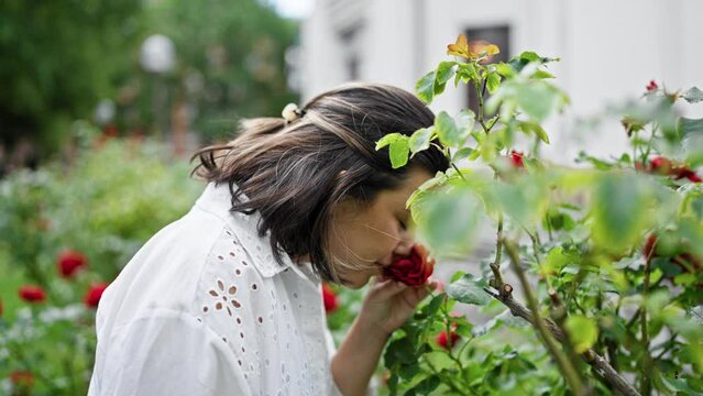 Beautiful young hispanic woman smelling red roses at the park