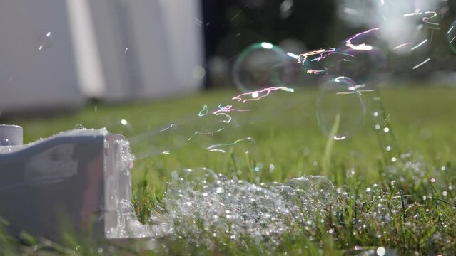 Slow motion of bubble maker machine at outdoor wedding tent blowing soap and water into bubbles into the sunny backlit air and wind