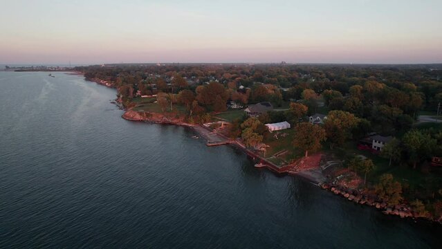 Drone shot and aerial of golden hour and bright sun above water's edge and suburban houses in neighborhood on Great Lake Erie shoreline in Lorain, Ohio near Cleveland and Sandusky