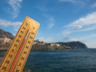 Wooden thermometer with red measuring liquid showing high temperatures on sunny day on background of seaside. Concept of vacation, holiday, warm weather, global warming, climate change.