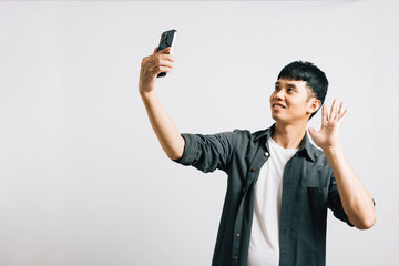 Smiling Asian man captures the moment with a selfie on his smartphone in a studio shot on white background. Self-expression and fun photography, hello to the world