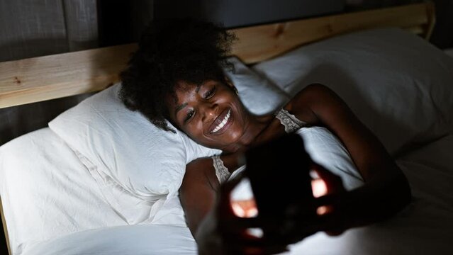 African american woman wearing lingerie using smartphone lying on bed at bedroom