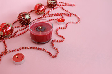 red Christmas ornaments, burning candles, beads diagonal lie on a pink background. Festive...