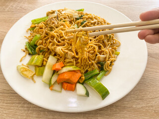 Chicken fried noodle with cucumbers salad on white ceramic plate and a chopsticks