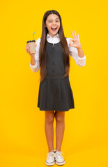 Amazed teen girl. Teenager girl holding a hot cup of coffee or tea. Child with takeaway cup on yellow background, morning energy drink beverage. Excited expression, cheerful and glad.