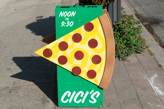outdoor sandwich or A frame board with wooden pizza slice, hours of operation, and name of CiCi's Pizza & Wings located at 1596 Queen Street West, Toronto, Ontario