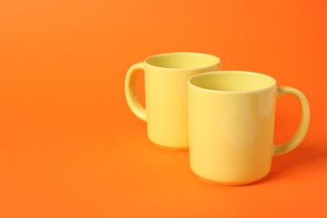 Two yellow ceramic mugs on orange background, space for text