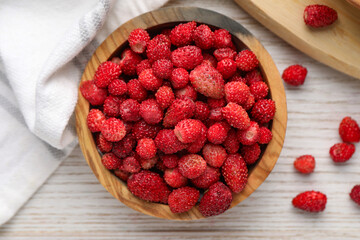 Fresh wild strawberries in bowl on white wooden table, flat lay