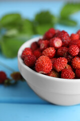 Fresh wild strawberries in bowl on light blue table, closeup