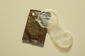 Unrolled female condom and package on beige background, above view. Safe sex