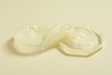 Unrolled female condom on beige background, closeup. Safe sex